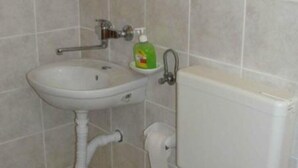 A bathroom with a white sink, a green bottle of liquid soap, and a white toilet. - Apartments Boguvila - One-bedroom Apartment With Terrace - (Supetar)