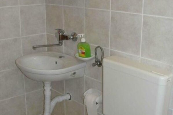 Une salle de bain avec un lavabo blanc, un flacon de savon liquide vert et des toilettes blanches.