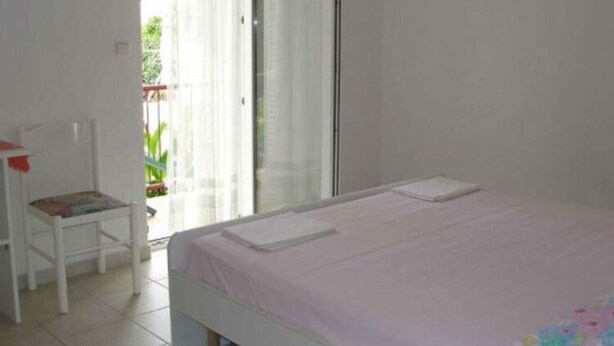 A bedroom with a bed, a chair, and a window with a view of greenery outside. - Apartments Boguvila - One-bedroom Apartment With Terrace - (Supetar)
