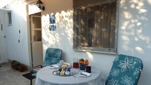 Una mesa redonda con mantel de encaje, dos sillas con tapicería floral y una ventana con marco de metal.