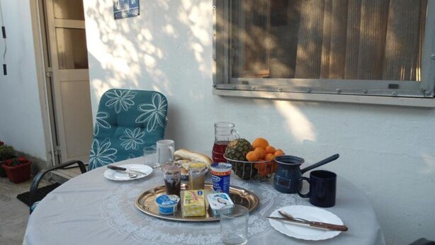 Una mesa redonda con mantel blanco, una bandeja metálica con comida, una jarra de vidrio y una taza azul.