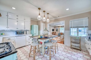 A kitchen with white cabinets, a gas stove, a microwave, and a dining area with stools.