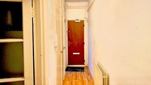 A narrow hallway with a wooden floor, a red door at the end, and a welcome mat. - Attractive Tower Bridge Apartment! 2 mins from the river side! (LONDON)