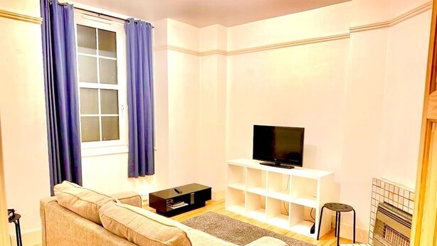 A living room with a sofa, a TV on a stand, a fireplace, and a window with curtains. - Attractive Tower Bridge Apartment! 2 mins from the river side! (LONDON)
