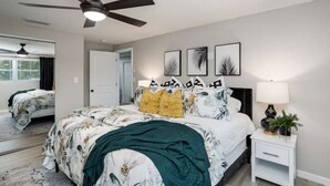 Une chambre à coucher comprenant un lit, une table de chevet, un ventilateur de plafond et des œuvres d’art murales.