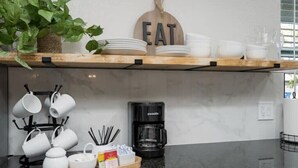 Une cuisine avec une étagère en bois où sont rangées des assiettes, des bols et une machine à café.