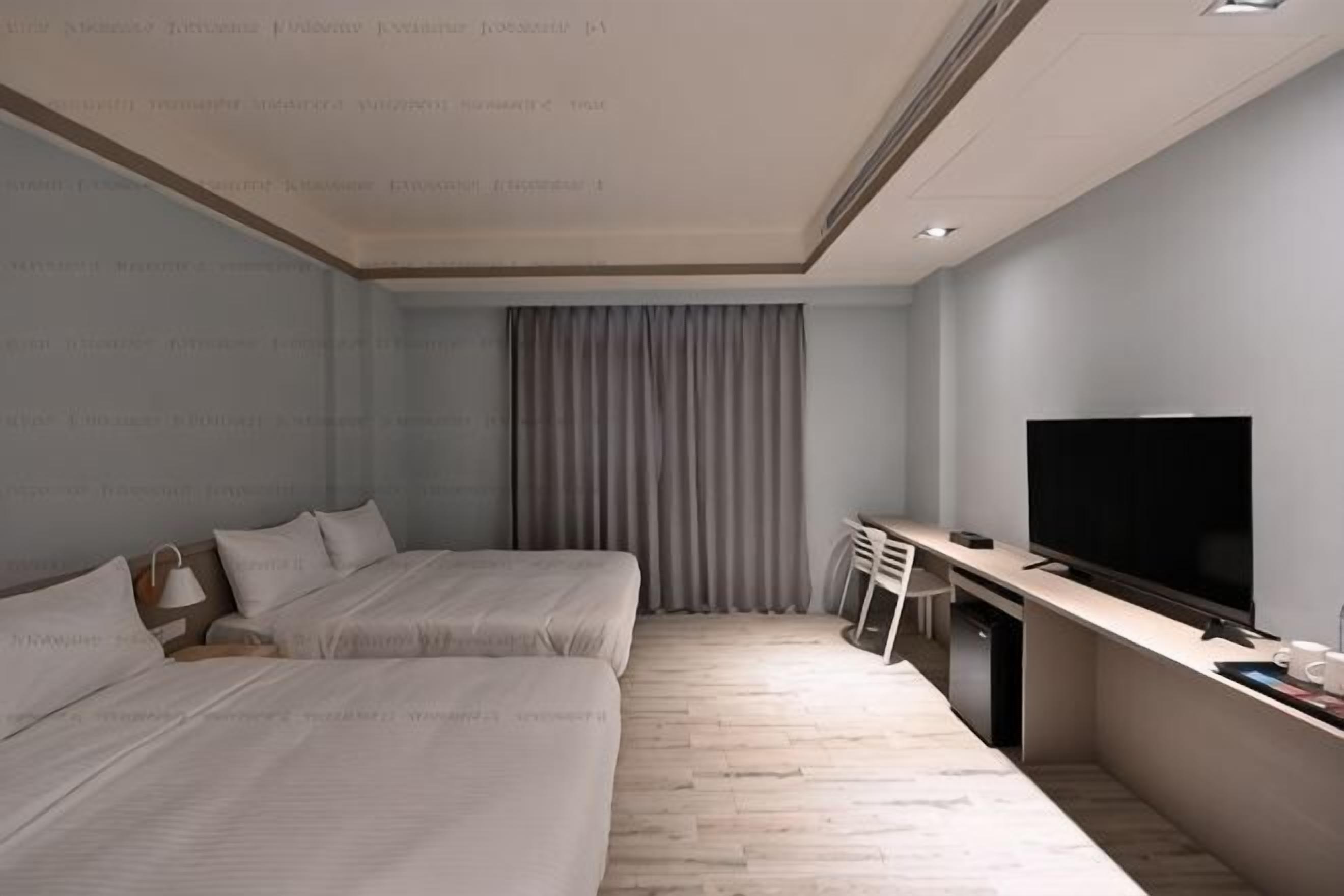 Una habitación de hotel con dos camas, un escritorio, un televisor y una ventana con cortinas.