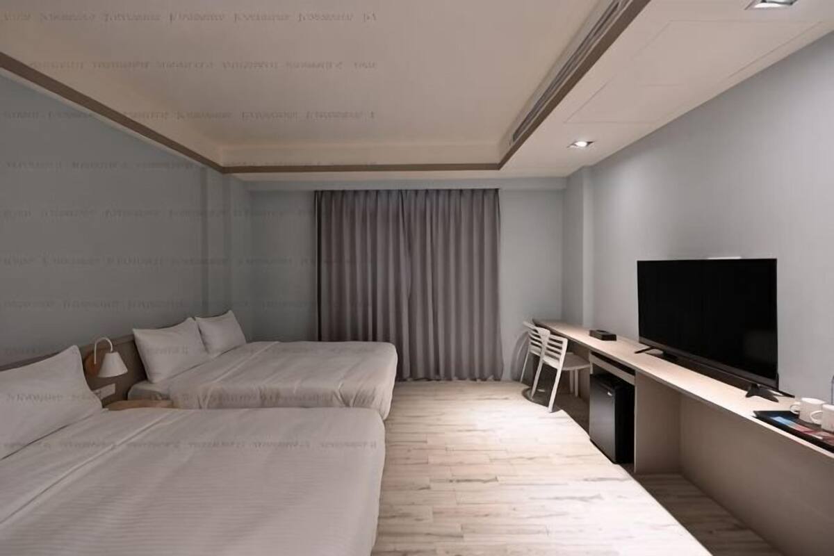 Een hotelkamer met twee bedden, een bureau, een televisie en een raam met gordijnen.
