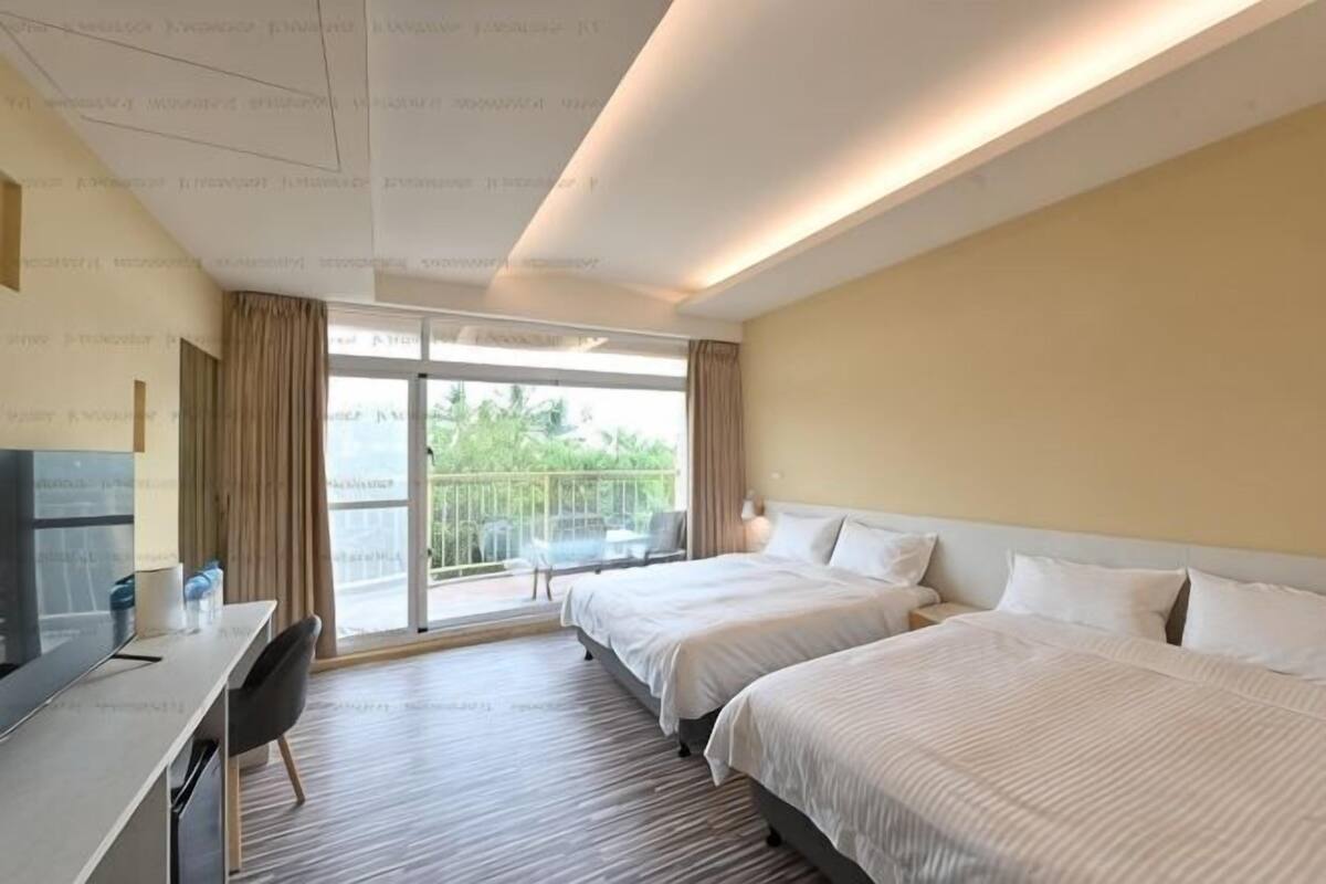 Een hotelkamer met twee bedden, een bureau, een stoel en een balkon met uitzicht.