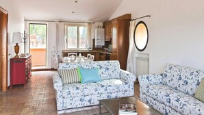 Un salon spacieux avec deux canapés  à motifs floraux, une table basse et un coin repas avec une table dressée pour quatre personnes.