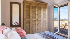 Une chambre à coucher comprenant un lit, une armoire, un miroir et une porte-fenêtre coulissante donnant sur un espace extérieur.