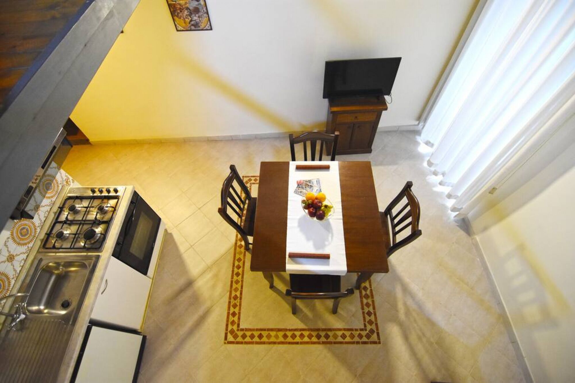 Un coin repas avec une table dressée pour deux personnes, une cuisine équipée d’une cuisinière et d’un évier, et un escalier menant à l’étage supérieur.