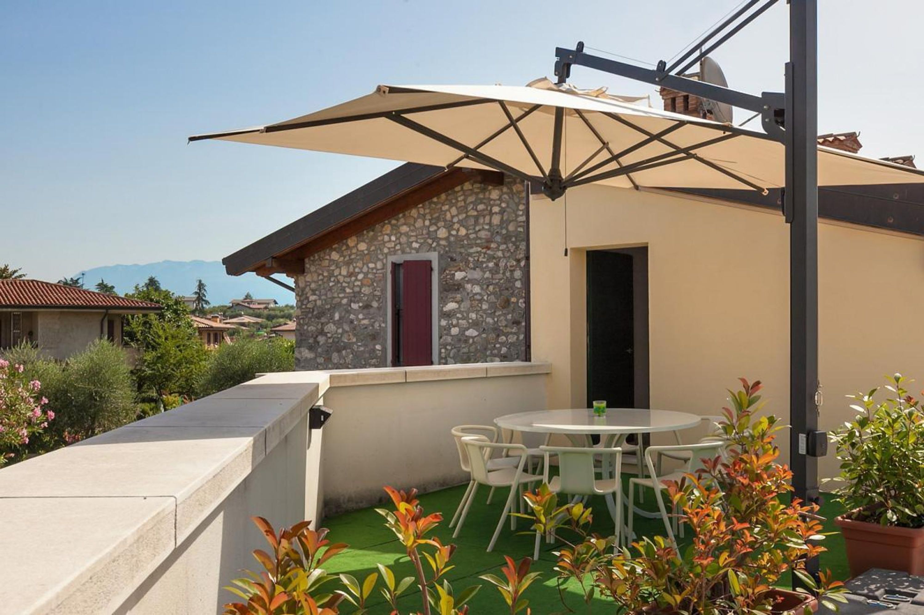 Una casa pequeña con fachada de piedra, techo verde y un patio con mesa y sillas.