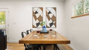 Un espace repas comprenant une table en bois, des chaises noires et deux œuvres d’art abstraites accrochées au mur.