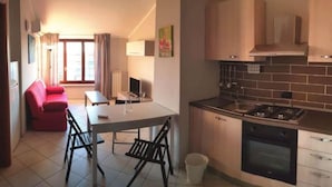 Une cuisine compacte équipée d’une cuisinière, d’un four et de meubles de rangement modernes. On y trouve un coin repas avec une table et des chaises, ainsi qu’un canapé rouge à l’arrière-plan.