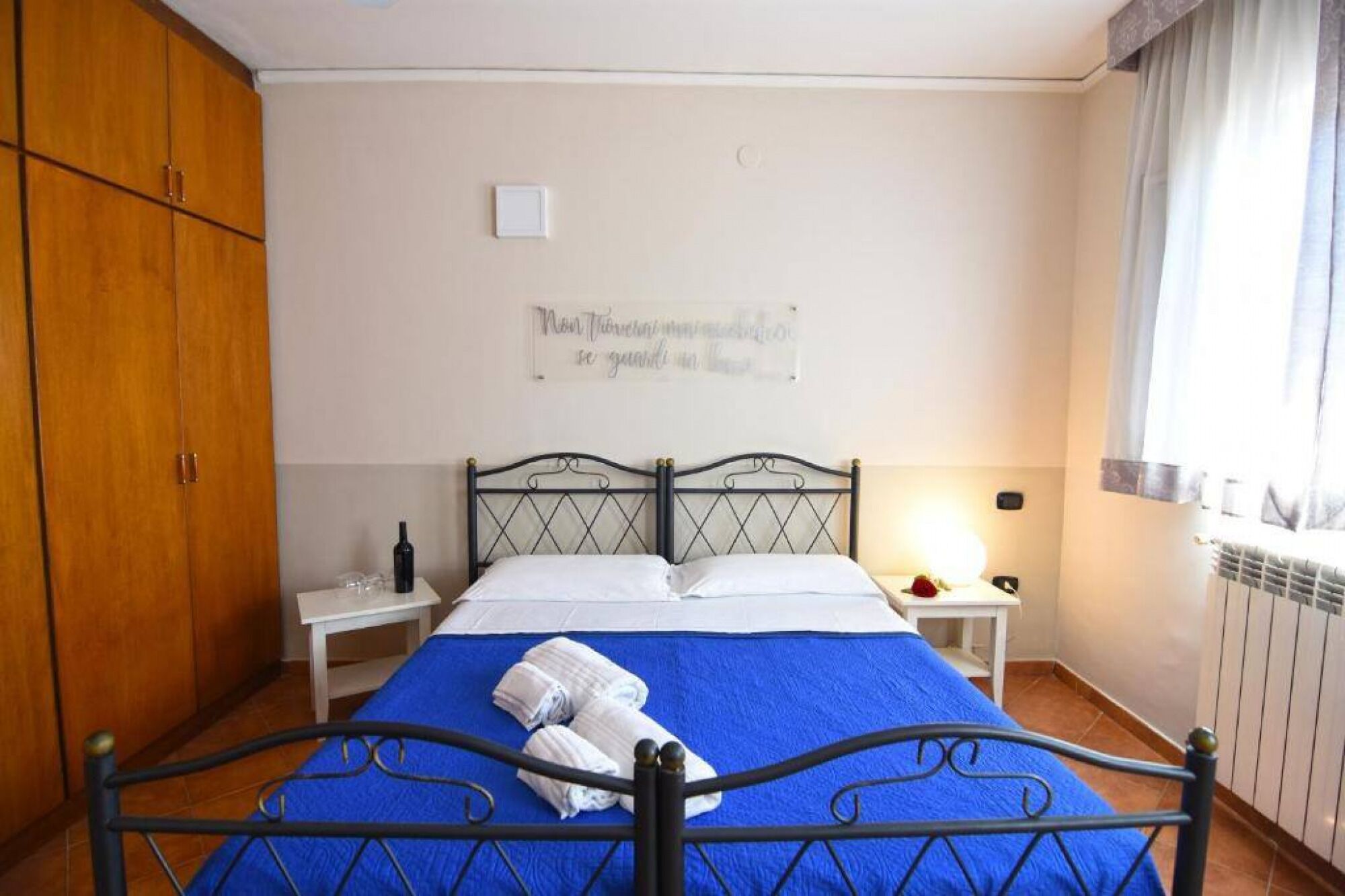 A bedroom with a bed, a nightstand, a lamp, a radiator, and a wardrobe.