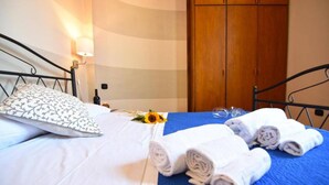 A neatly made bed with a floral pillow, a blue blanket, and rolled towels. - Case Cosi Napoli - APP 17 (Naples)