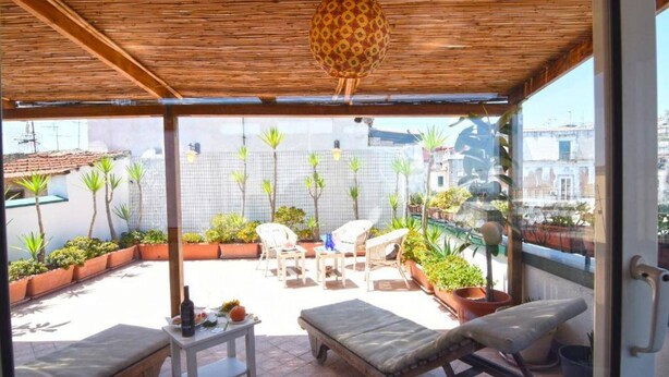A covered outdoor patio with lounge chairs, a small table with drinks, and potted plants. - Case Cosi Napoli - APP 17 (Naples)