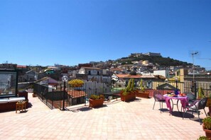 A rooftop terrace with potted plants, outdoor seating, and a view of a hilltop building. - Case Cosi Napoli - APP 7 (Naples)
