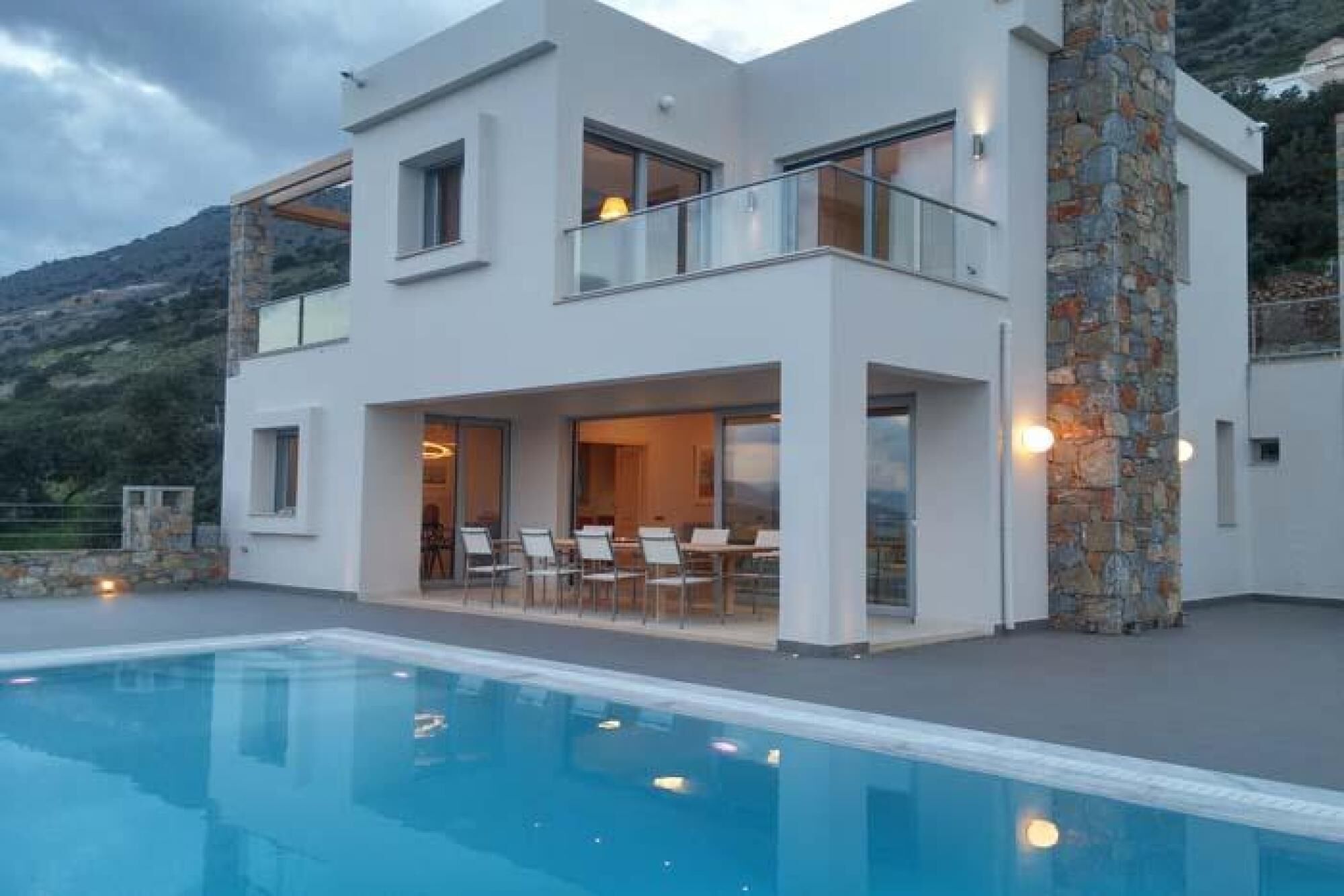 A modern two-story house with a swimming pool, large windows, and a stone exterior.