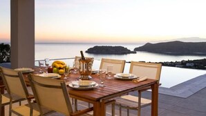Une table à manger dressée pour quatre personnes, avec vue sur la mer et les collines.