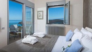 Une chambre à coucher avec un lit, une fenêtre donnant sur la mer, un radiateur et une chaise près de la fenêtre.