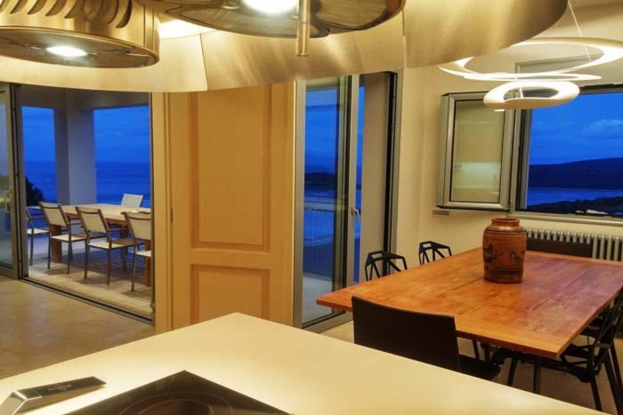 Een moderne eetruimte met een grote tafel, stoelen en uitzicht op de zee door grote ramen.