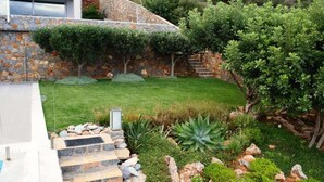 Une maison moderne avec une façade en pierre, une pelouse bien entretenue et une variété de plantes et d’arbustes.