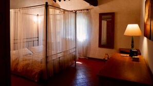 Una cama con dosel y cortinas translúcidas, una mesita de noche de madera con una lámpara, y un espejo en la pared.