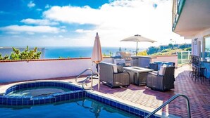Un área de piscina en la azotea con vista al océano, mobiliario exterior y una parrilla.