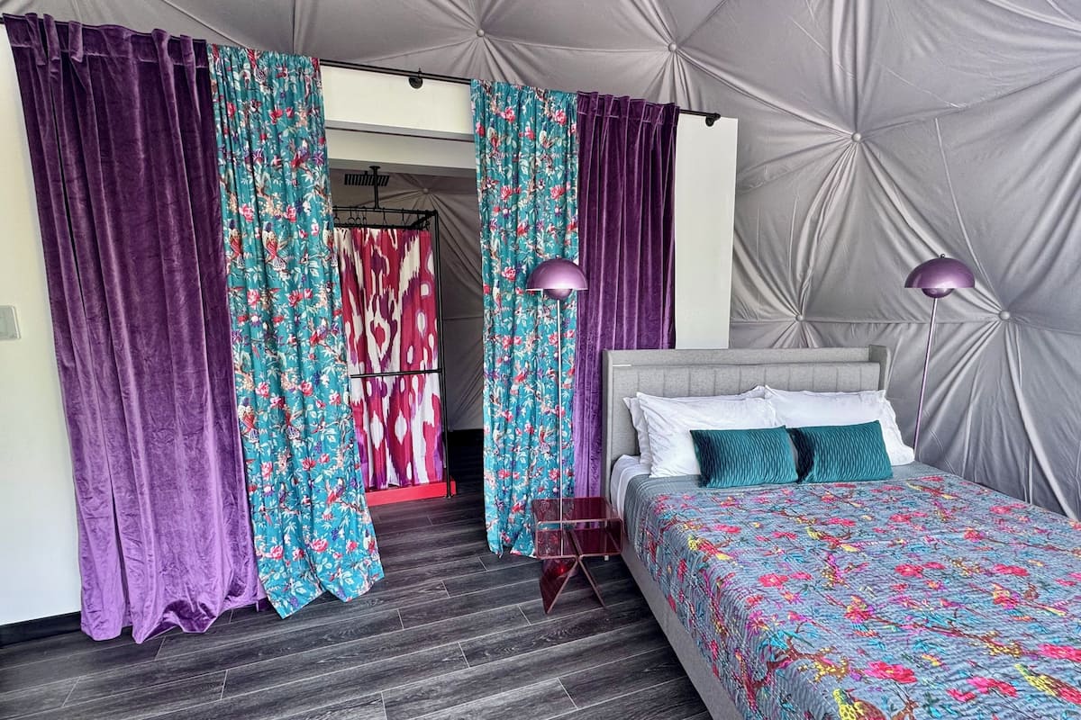 A bedroom with a bed, purple curtains, a wardrobe, and a floor lamp.