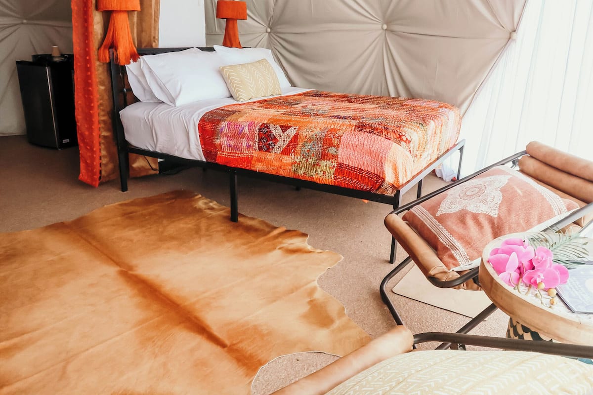 A cozy room with a bed, a chair, a small table, and a large, padded wall.