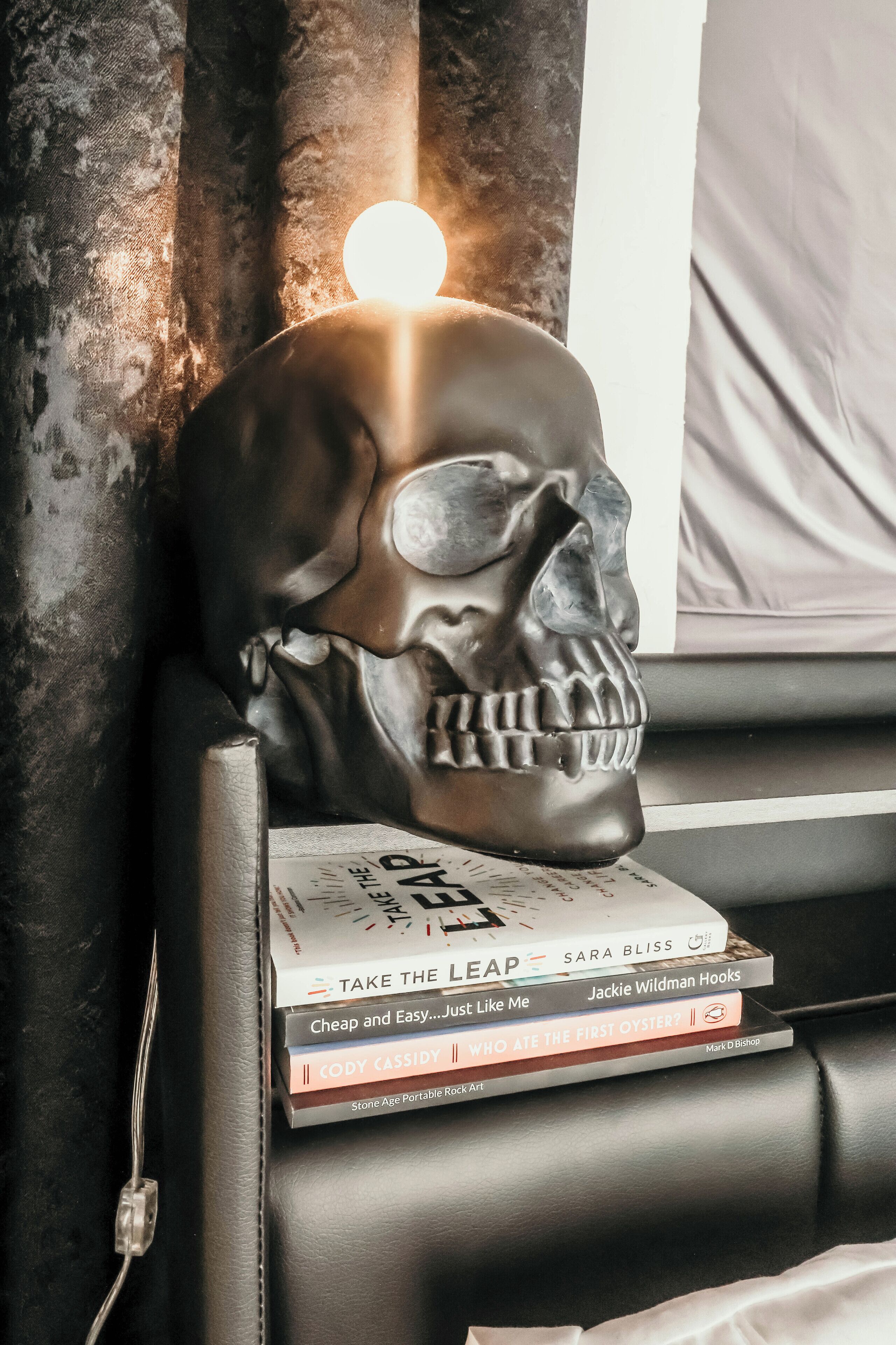 Une sculpture de crâne est posée sur un canapé en cuir noir, à côté d’une pile de livres.