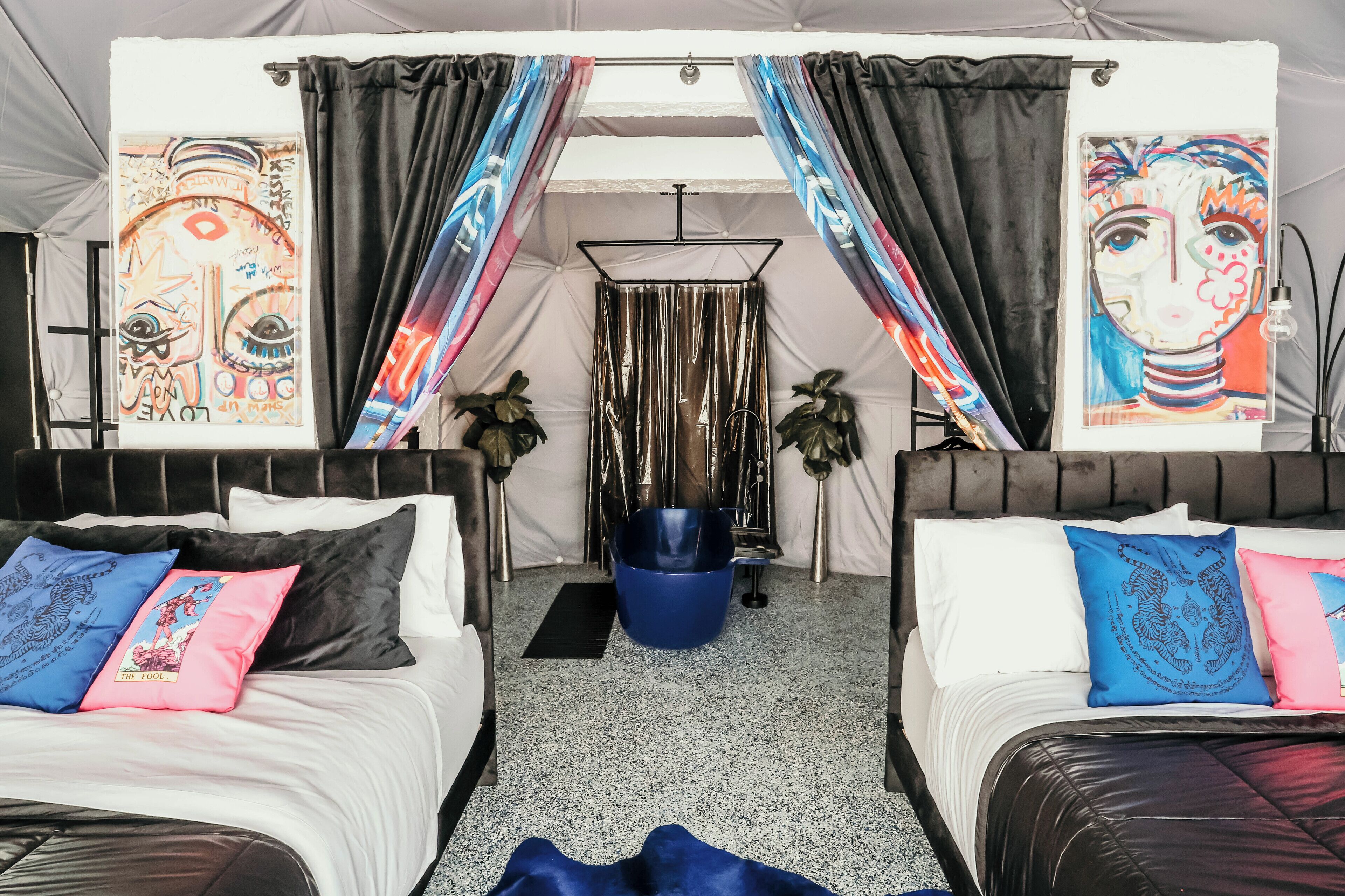 Ein Zimmer mit zwei Betten, beide mit weißer und schwarzer Kopfstütze, sowie einem Bereich mit einem blauen Sessel und einer schwarzen Fußmatte.