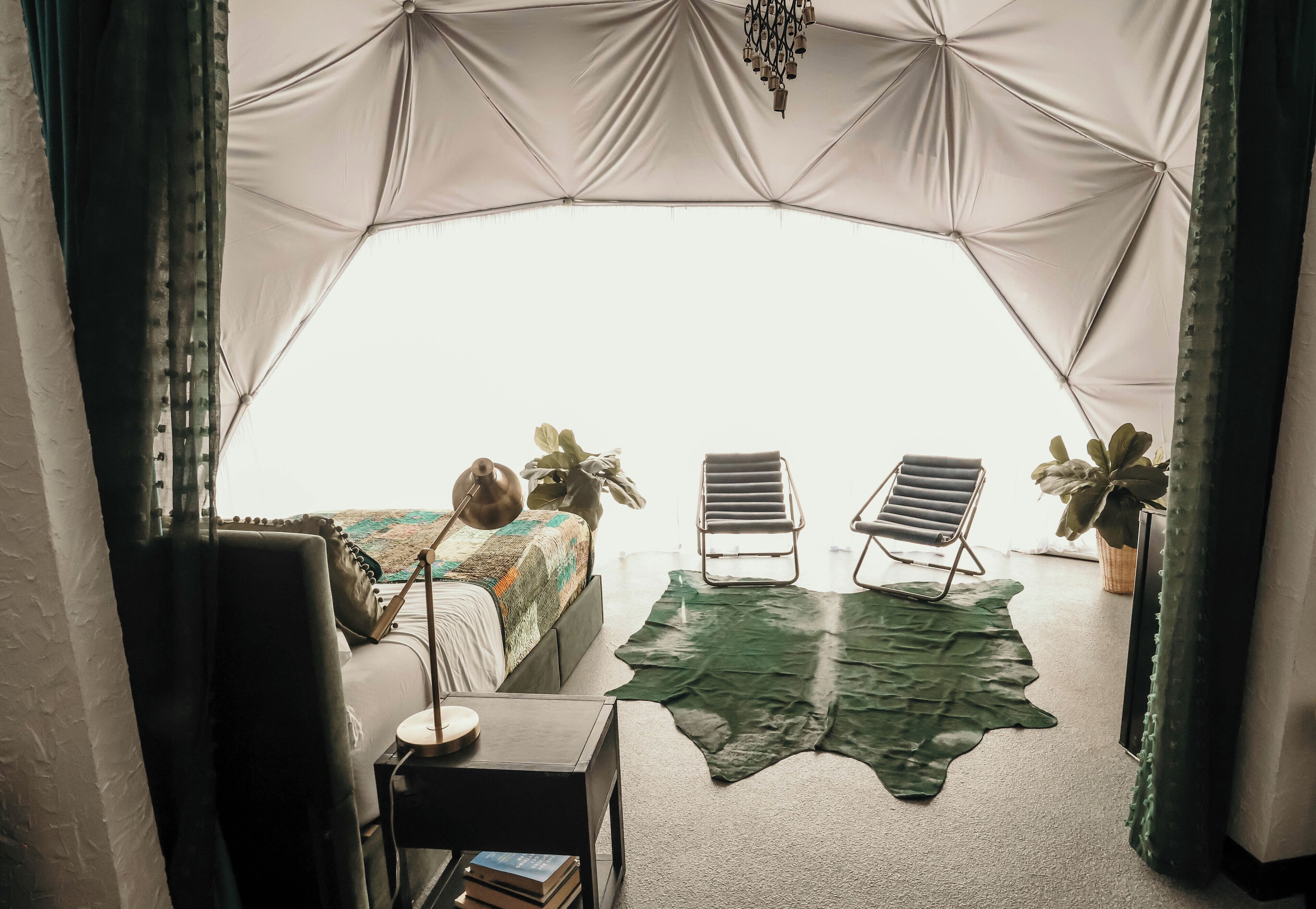 Una habitación con tienda de campaña, una cama, dos sillas, una mesita y una alfombra verde.