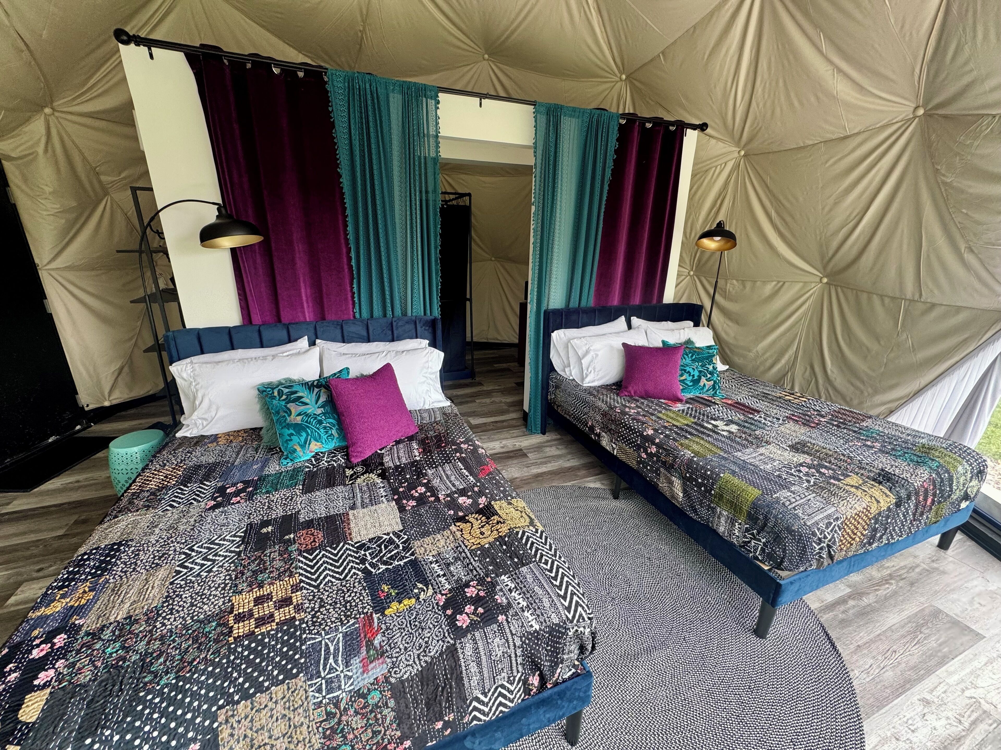 A tented accommodation with two beds, each with patterned quilts and pillows, and a view of the outdoors.