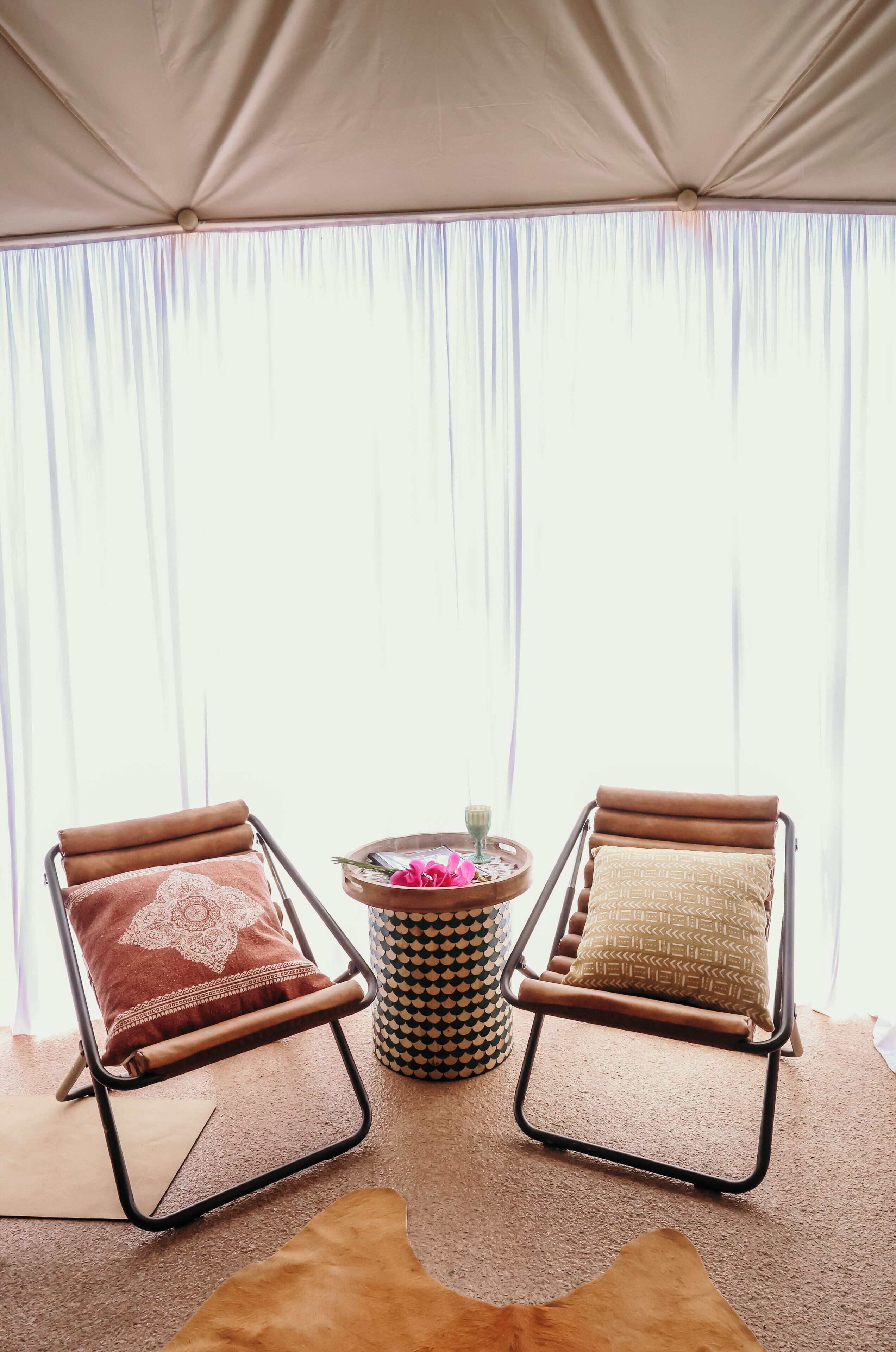A room with two leather armchairs, a round table with a patterned rug, and a large window with sheer curtains.