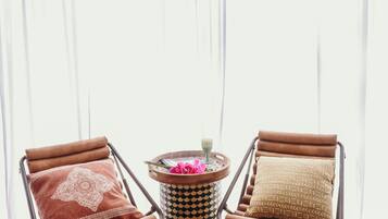 A room with two leather armchairs, a round table with a patterned rug, and a large window with sheer curtains.