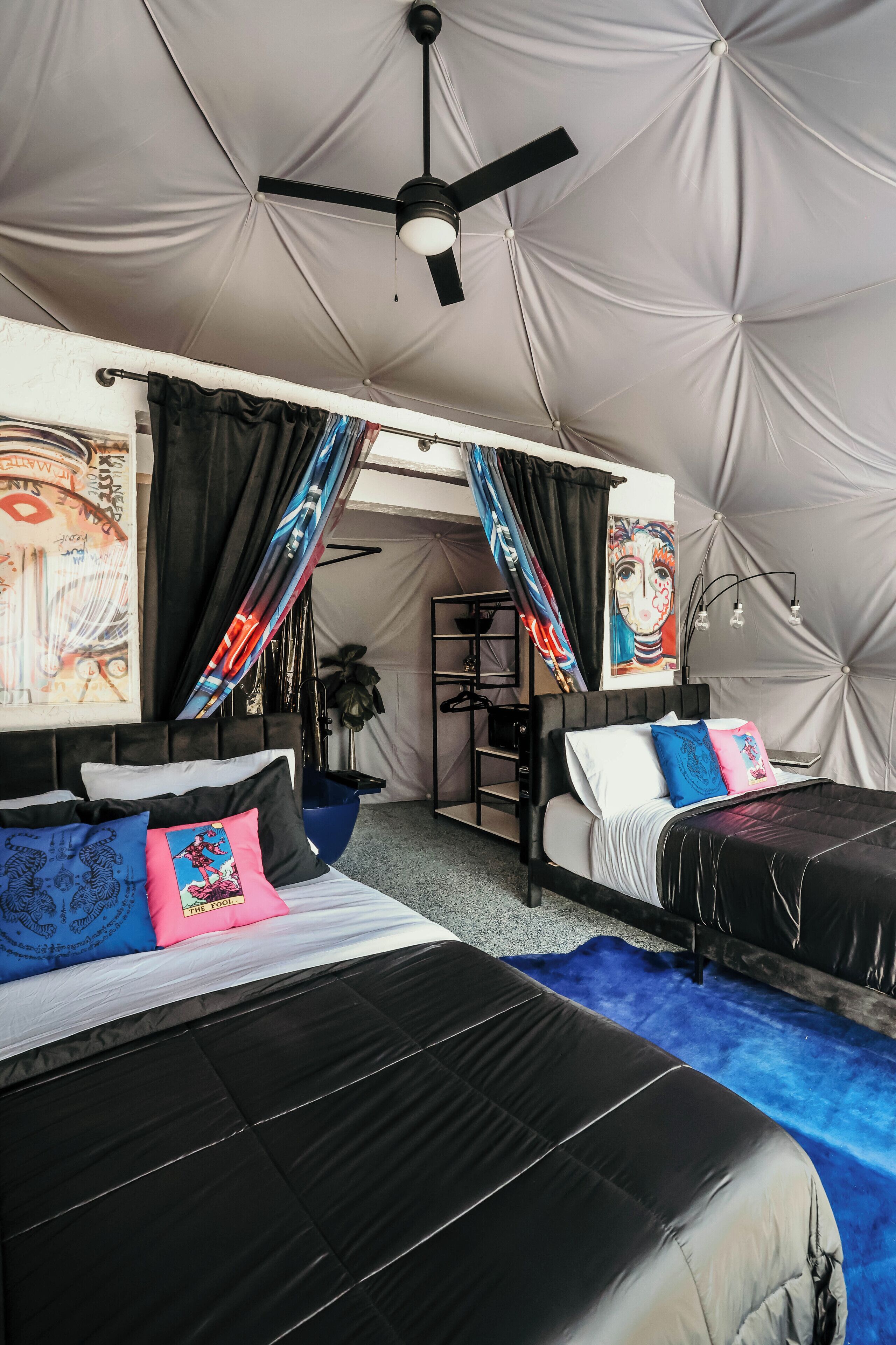 A tent-style room with two beds, a ceiling fan, and artwork on the walls.