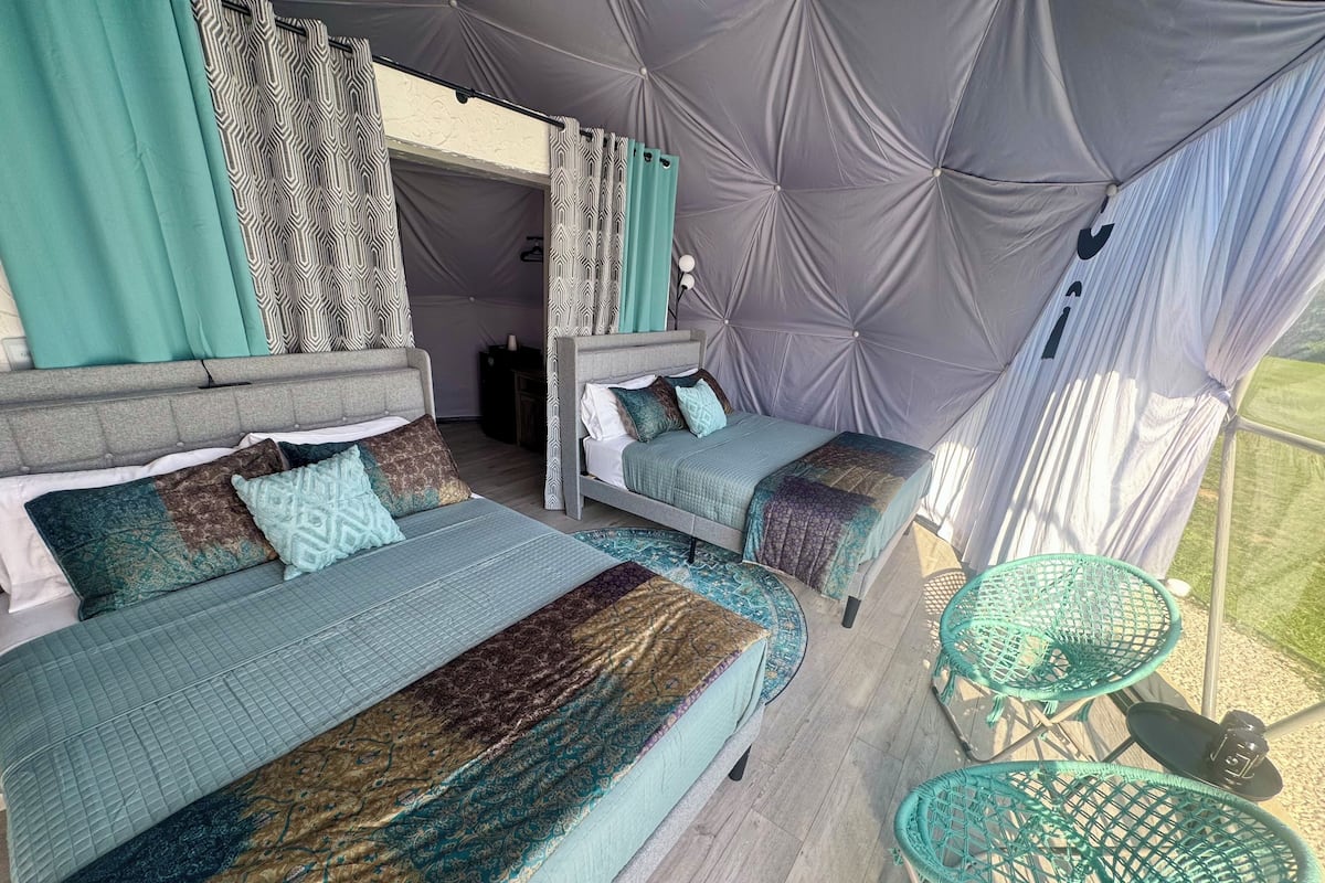 A tented accommodation with two beds, patterned bedding, and a green chair.