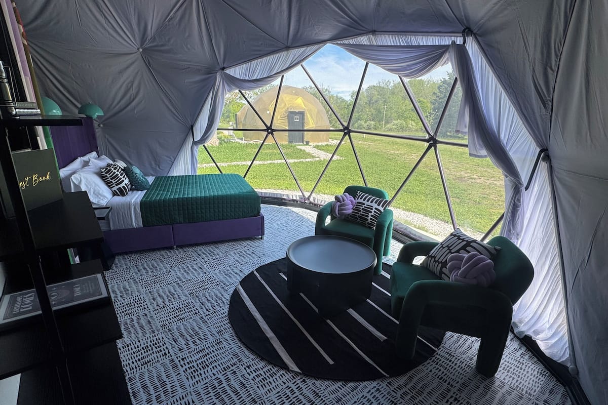 A tented accommodation with a bed, a small table, and a chair.