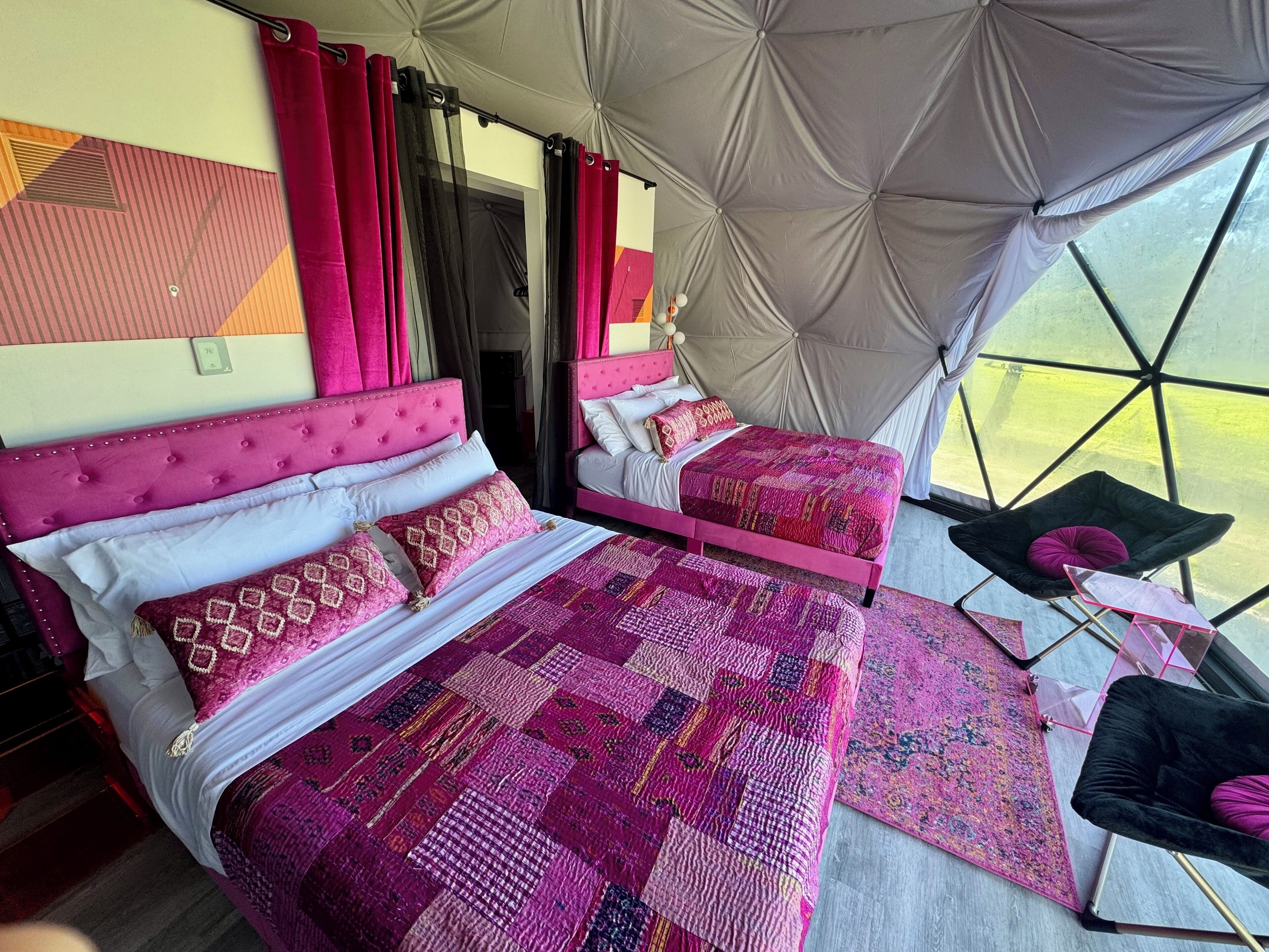 Una habitación tipo tienda de campaña con dos camas, cada una con cabecero rosa y ropa de cama estampada.