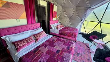 Una habitación tipo tienda de campaña con dos camas, cada una con cabecero rosa y ropa de cama estampada.