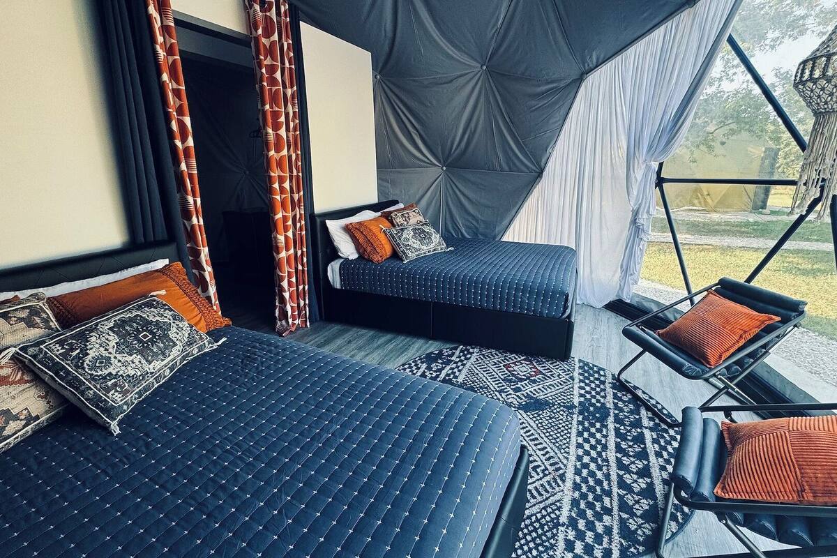 A cozy room with two beds, a chair, and a hanging light fixture.