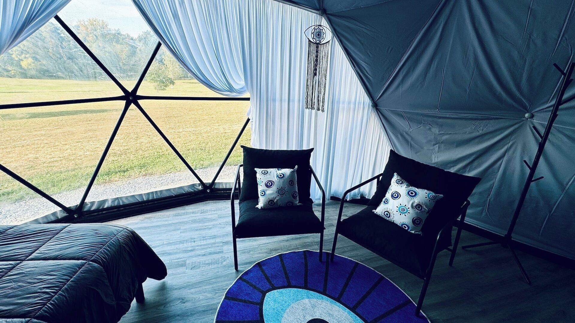 A tented room with a bed, two chairs, and a view of the outdoors.