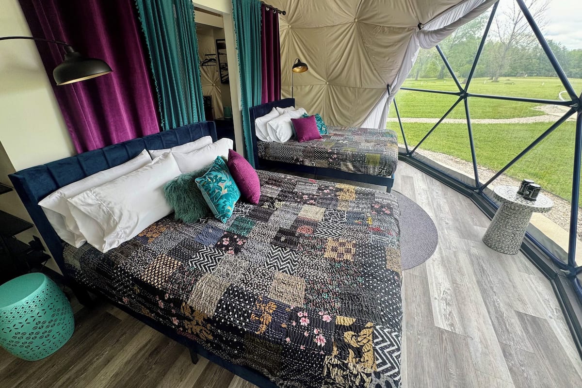 A bedroom with two beds, a large window, and a view of a grassy field.
