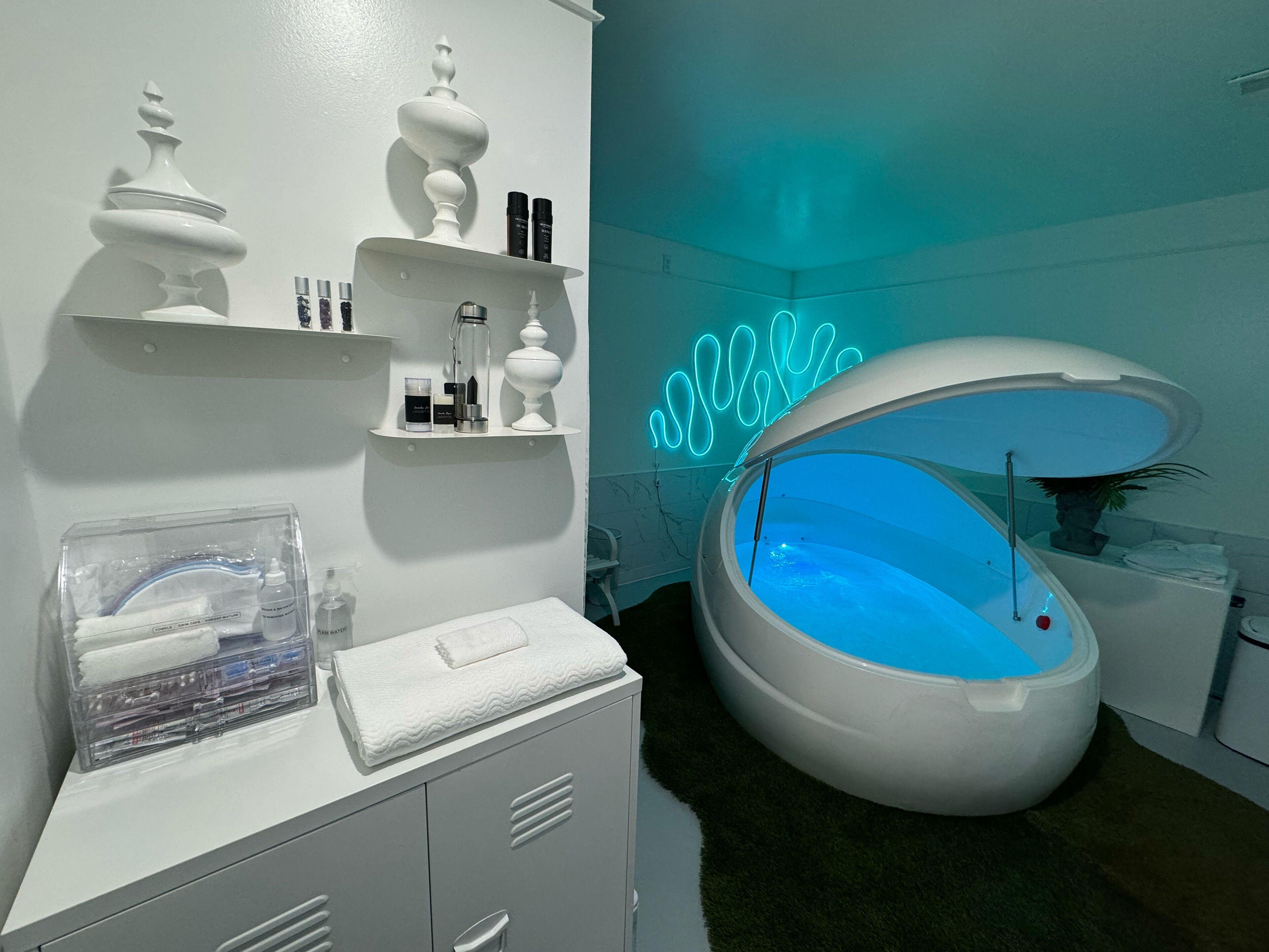 A modern bathroom with a freestanding bathtub, shelves with toiletries, and a neon light.
