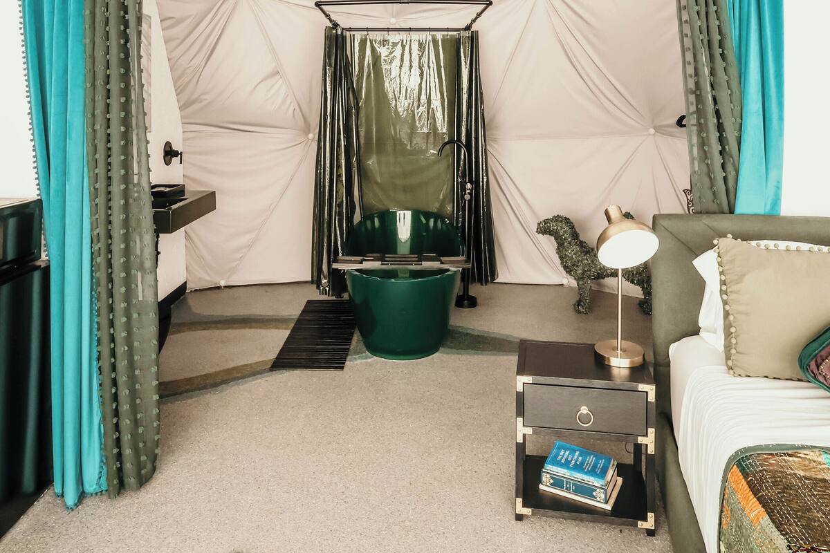 A tent-style room with a bed, a small table, a hanging chair, and a ceiling fan.