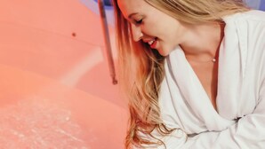A person in a white robe sitting in a bathtub with a pinkish water color. - DayDreamer Domes (South Haven)