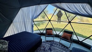 A tent with a bed and two chairs facing a grassy area with a decorative lamp. - DayDreamer Domes (South Haven)